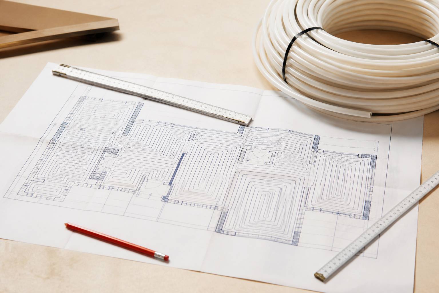 Plan A3 d'installation de chauffage au sol déplié sur une table d'atelier avec règles et crayon